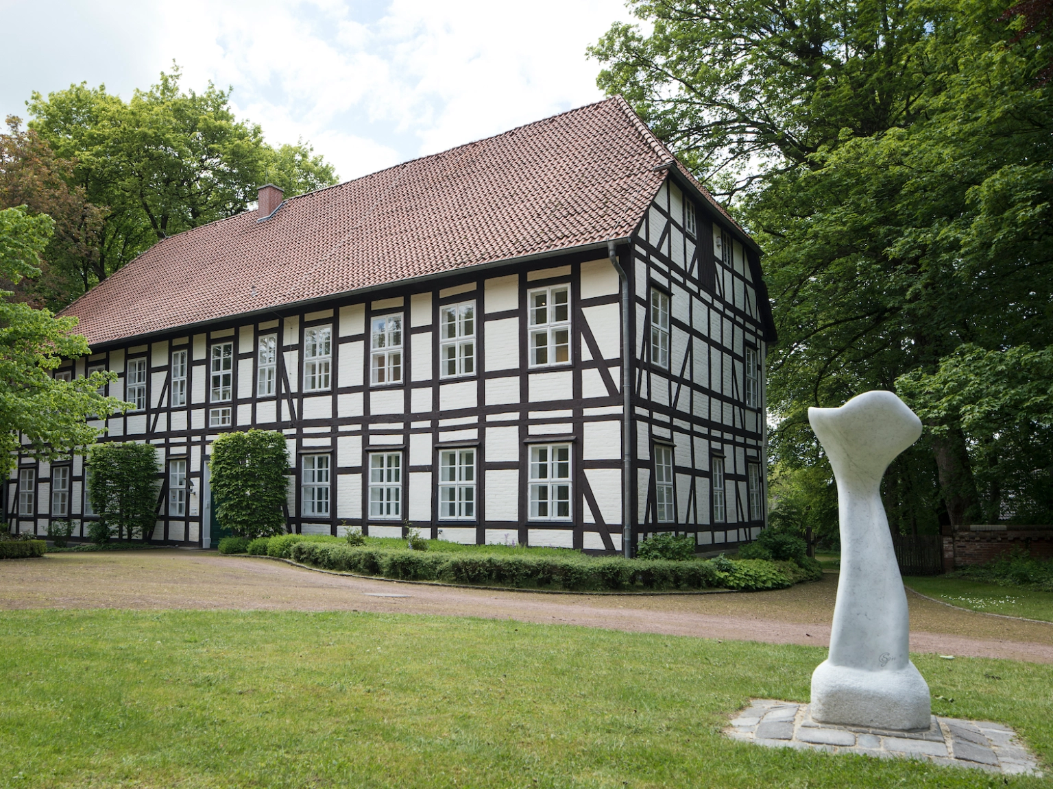 Außenansicht des syker Vorwerk. Ein herrschaftliches Fachwerkhaus mit umgebenden Park. Vor dem Haus steht eine Skulptur.