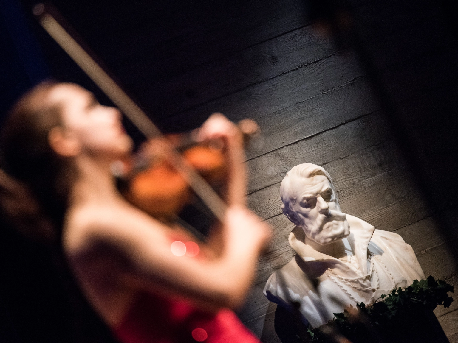 Impression des Joseph Joachim Violinwettbewerbs 2015 – im Vordergrund ein junge Geigerin im roten Kleid, im Hintergrund die beleuchtete Büste Joseph Joachims