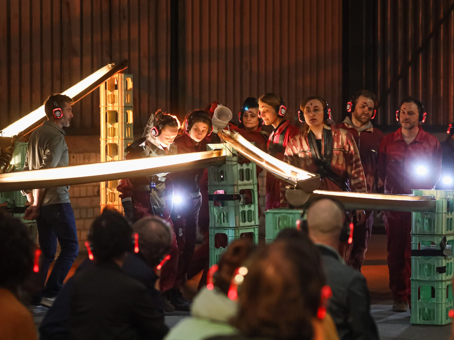 Impression der Aufführung I CALL IT WATER: #1 SPIRIT des Theater an der Glocksee beim Best OFF 2022. Eine Gruppe von Menschen steht um eine hellerleuchtete Wasserbahn aus Regenrinnen. Eine Person kippt mit einer Kanne Wasser hinein. Alle tragen Kopfhörer.