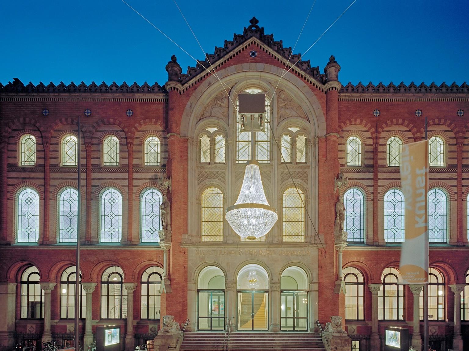 Das Künstlerhaus Hannover in der Sophienstraße. Auf dem Bild im sind alle Fenster hell erleuchtet. Vor dem Haus leuchtet die ikonische Kronleuchterskulptur „Das große Leuchten” von Stephan Huber.